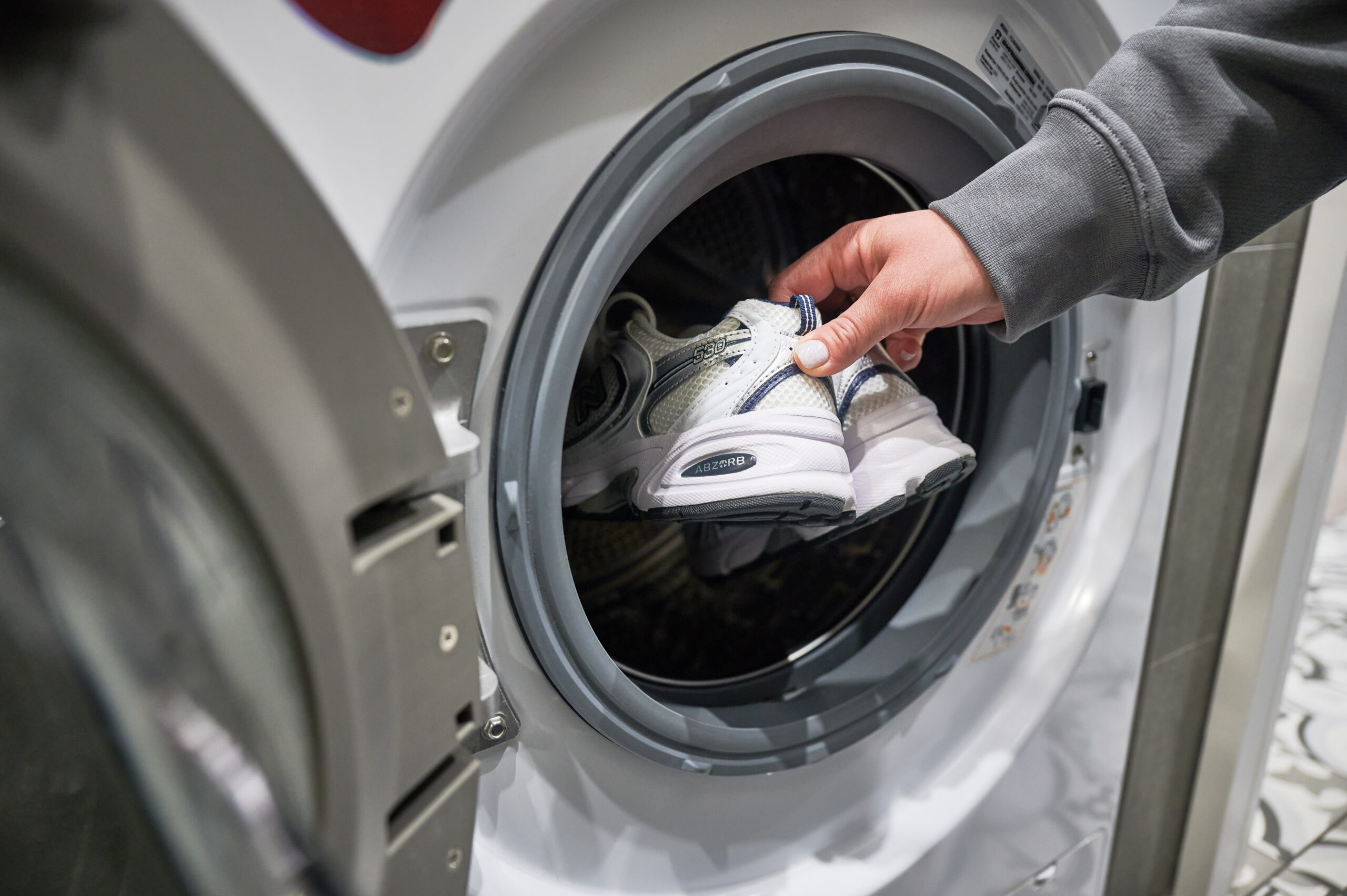 Lviv, Ukraine – May 7, 2023: Woman putting pair of sport shoes into washing machine. Lviv, Ukraine - May 7, 2023: Woman putting pair of sport shoes into washing machine. Washing white pair of New Balance 530 sneakers.