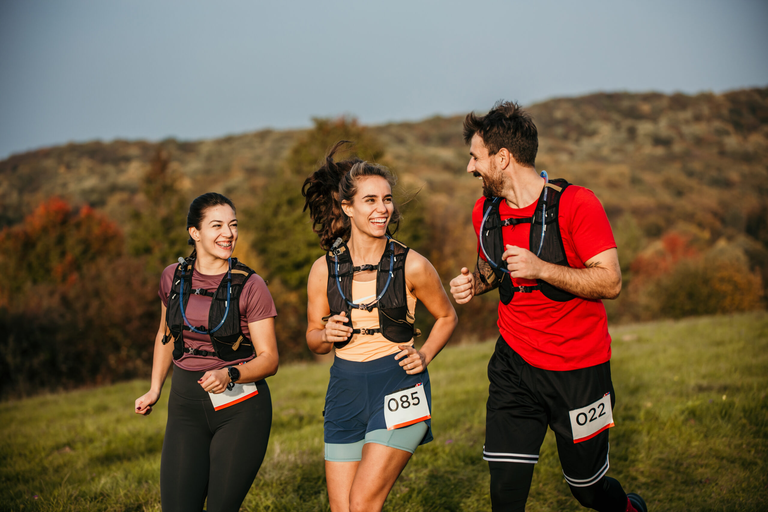 A small group of adults running in an outdoor cross-country race together. They are each dressed comfortably in athletic wear and have numbers pinned to the front of them as they focus